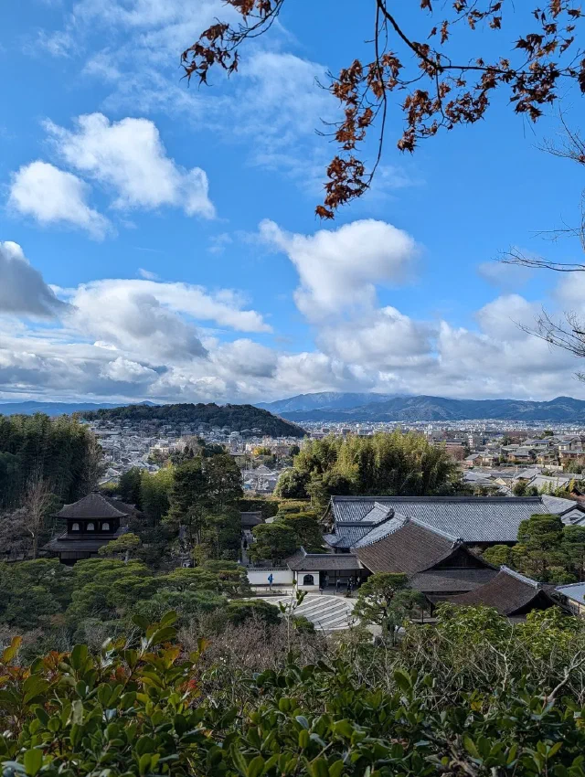 從銀閣寺庭園眺望京都，遠處是山景，前景是寺院屋頂與樹木。
